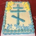 Photo of the cake for St Michael's Day. The cake has white icing with light blue dollops around the edges, a light blue Russian cross in the center, and the words St. Michael's below the cross. Flowers made of yellow icing appear in the top left and right corners, within the blue dollops.