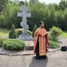 Photo of Father Vjekoslav holding a bible and censor and praying, with his back facing a large concrete cross in St. Michael's Cemetary