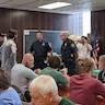 A portion of the church hall, where parishoners and guests are seated at tables. Two police officers are talking with Fr. Vjekoslav, the parish priest.