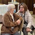 Photo of two seated women talking. The woman on the left has short, gray hair and is wearing a brown jacket, light gray pants, black glasses, and a surgical mask. The woman on the right has shoulder-length, brown hair and is wearing an off-white puffer coat, dark gray slacks, and black glasses.