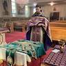 Photo of Father Vjekoslav standing before a table with green vestments. He's holding a prayer book, preparing to bless the vestments.