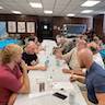 Parishioners are still at tables talking. There are three tables running from foreground to background. The center table has an off-white tablecloth, and the tables on either side has bright, sky-blue tablecloths.