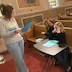 Photo three tweens sitting the front pew during Sunday school. The female Sunday school instructor is standing in front of three students, who are seated in the first pew, and to the left of frame. She is holding and reading from a blue folder.