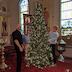 Three men are decorating a Christmas tree at the front of the church. The iconostas appears behind them.