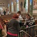 Three woman in the foreground are decorating a railing with green garland while five people in the far background, at the front of the church, decorate the Christmas tree.