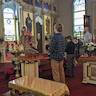 Father Fravel stands in front of the Royal Doors, presenting the gifts to the congregation. An alterboy, holding a large candle, stands at the bottom of the three steps and has a man on either side of him. The men are also holding candles.