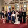 The bride and groom pose for a photo in front of the iconostas, and they are surronded by eight loved ones, including two young girls and a priest.