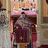 Father Barnabas Fravel, wearing a purple vestment with gold embellishments, is standing at a lecturn in front of the altar, facing the congregation during the Palm Sunday service.