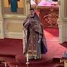 Father Barnabas Fravel is standing in front of the altar, facing the congregation, and is holding a cross.