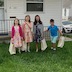 Four kids (three girls and a boy) pose for a picture on the lawn of the rectory. They're each holding a bag of the treasures they found during the Easter egg hunt.