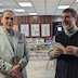 A male parishoner and Fr. Barnabas pause their converstation in the church all to pose for a photo. Fr. Barnabas is on the right and is holding a book.