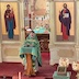 Wearing green vestments, Father Barnabas Fravel stands at a lecturn in front of the Royal Doors and addresses the congregation.