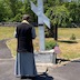 Fr. Barnabas is standing outside, in front of a large, white cross at Sts. Peter and Paul cemetery in Centralia. His back is facing the camera.