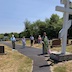 Fr. Barnabas is standing outside, in front of a large, white cross on a small pedestal, at Sts. Peter and Paul cemetery in Centralia. Four parishioners are seen standing about ten feet behind him.