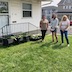 Three woman stand in the back yard, posing next to the plants they've just potted. A few neighborhood houses appear in the background.