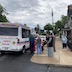 A different view of the line of people waiting for treats from Pepe's ice cream truck, which appears in the left third of the photo. The photo shows the back of the truck, and the chuch is seen in the right third of the frame. The line runs in the middle of the frame, from right to left.
