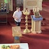 Father Barnabas exits an altar door while holding the Royal Gifts. An alter server, holding a candle, stands to the side of the door while another server, who is also holding a candle, leads the way.