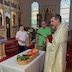 Father Barnabas is blessing vegetables and fruit in a basket on a table that is covered with a white table cloth. 