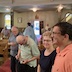 View from the front of the church looking back towards the pews. There's a man and a woman smiling in the lower right corner, with two men to their right. Other parishioners can be seen further left and to the back, and there's a woman in the choir loft who appears in the upper right hand corner of the frame. Fr. Aleksey is walking towards the back of the church.