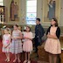 A group of five children are standing in a row alongside pews. There are three younger girls on the left, then a slightly older boy, and a teenage girl on the right.