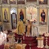 Father Aleksey, Father Timothy, and Father Vjekoslav standing in front of the Royal Doors and presenting the Holy Gifts to the congregation. Father Aleksey is wearing gold-colored vestments, Father Timothy is wearing bronze-colored vestments, and Father Vjekoslav wearing white vestments. Two altar boys are also visible in the lower left portion of the frame.