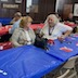 View of the center table, which is covered by a blue tablecloth and now mostly empty. The photo was taken from an angle that has the table running from the lower left corner to roughly the middle of the right edge of the frame. There are two women sitting on the far side of the table and talking to each other. Three men are visible in the background and are seated at the red table behind them.