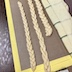A close-up of three dough-rope braids on top of a Silpat mat. A towel that is mostly off-white, but with thin green and gray strips, is rolled up flatly and runs along the length of the braids. A few specks of black, which I believe to be poppy seeds, are visible within the braids.