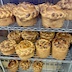 A three-level metal rack with complete paska breads that I believe are cooling. The top row appears to be just below eye-level and shows mostly the sides of the loaf, whereas the two rows below have views looking mostly down at the loaves. Six loaves are visible on top rack, eight in the middle, and five on the bottom, although there are likely more loaves that can't be seen in the photo.