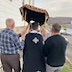Four men outside, carrying the Epitaphios (a large, embroidered and often richly adorned cloth, bearing an image of the dead body of Christ) in a procession around the church. The view is from behind the men, and Fr. Aleksey is walking in the middle, under the Epitaphios, but at the moment, is mostly between the two men in back. The man at the front left is only slightly visible.