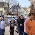 Procession of parishioners walking under the Epitaphios as they re-enter the church, at the end of the procession. Part of one of the wooden doors is visible in the upper right, and neighborhood houses and cars fill the background.