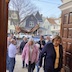 More parishioners are walking under the Epitaphios as they re-enter the church, at the end of the procession. Part of one of the wooden doors is visible in the upper right, and neighborhood houses and cars fill the background.