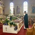 View of the tomb from the left side of the church. Fr. Aleksey is standing in front of the tomb, facing left, towards the iconostas, and he's reading from a prayer book. Light is streaming into the church through the stained glass windows in the background.