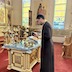 Fr. Aleksey is standing in front of the center table, which appears in the lower-left quarter of the photo. He's wearing a black cassock and is looking down at a black prayer book.