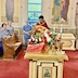 A side view of the center table with Fr. Aleksey standing on the far side. He's holding a censor and is blessing the items on the table. Three parishoners appear behind him and to his left, as they stand in the first and second pews. 