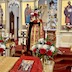 Fr. Aleksey stands a few feet in front of the open Royal Doors, and he's holding a cross in front of his head, presenting it to the congregation. The cross is on a small pedestal and is surrounded by red roses and white carnations plus a bit of greenery. Part of the iconostasis appears in the background, and the center table is partially visible in the foreground.