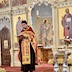 Fr. Aleksey is standing a few feet in front of the open Royal Doors. He's looking down at a book that he's holding. The photo was taken off-center to his left. The iconostasis appears in the background and part of the altar can be seen through the open doors.