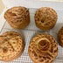 Five baked paska breads on cooling on metal racks on the kitchen counter. Three are completely visible, and the loave in the lower left is mostly visible. A small edge of the fifth paska bread is visible in the middle of the right-hand edge of the frame.